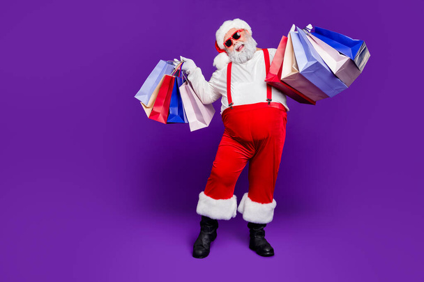 Full length body size view of his he nice cheery glad cheerful bearded thick fat Santa carrying bags new things clothing isolated over bright vivid shine vibrant violet lilac background - Фото, зображення