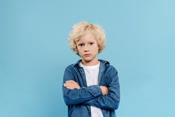 niño triste y lindo con brazos cruzados mirando a la cámara aislada en azul
  - Foto, Imagen