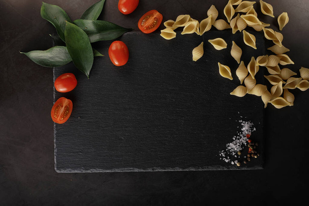Pasta shells on black stone. Tomatoes and bay leaves with allspi - Foto, imagen