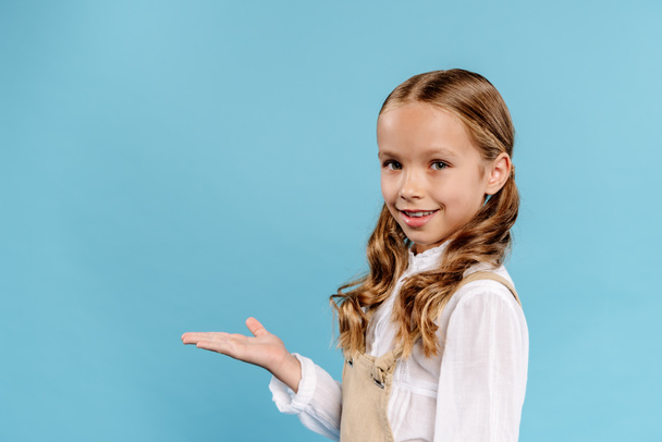 smiling and cute kid with outstretched hand looking at camera isolated on blue  - Foto, Bild