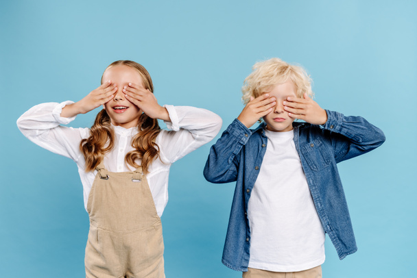 smiling kids obscuring faces with hands isolated on blue  - Фото, изображение