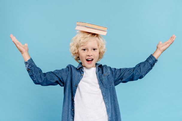 smiling and cute with books on head looking at camera isolated on blue  - Foto, imagen