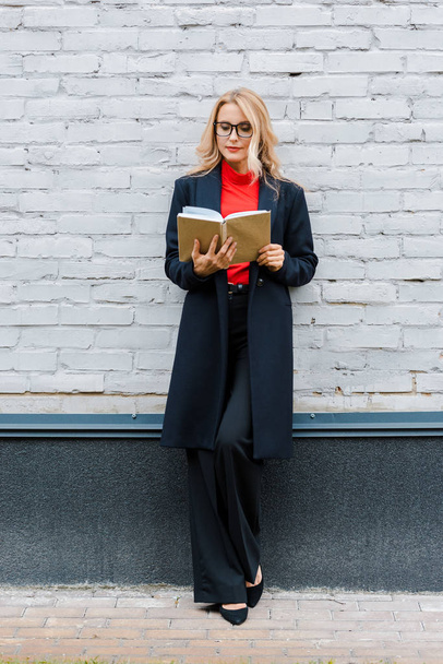 attractive businesswoman in black coat and glasses reading book  - Foto, Bild