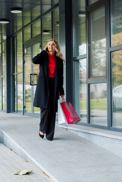 attractive businesswoman talking on smartphone and holding shopping bags - Zdjęcie, obraz