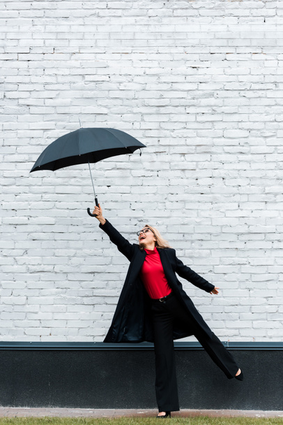 attractive businesswoman in black coat smiling and holding umbrella  - Фото, зображення