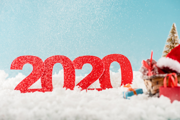 επιλεκτική εστίαση των αριθμών 2020 και λυγαριά έλκηθρο με χριστουγεννιάτικο δέντρο, κουτιά δώρων, τσάντες ψώνια στο παρασκήνιο  - Φωτογραφία, εικόνα