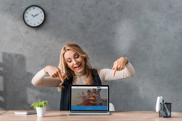 KYIV, UKRAINE - AUGUST 16, 2019: smiling businesswoman pointing with fingers at laptop couchsurfing website  - Foto, Imagen