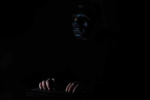 Чоловік у масці друкує на клавіатурі в темряві
 - Фото, зображення