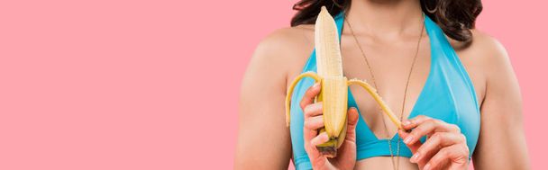 panoramic shot of young woman peeling banana isolated on pink  - 写真・画像