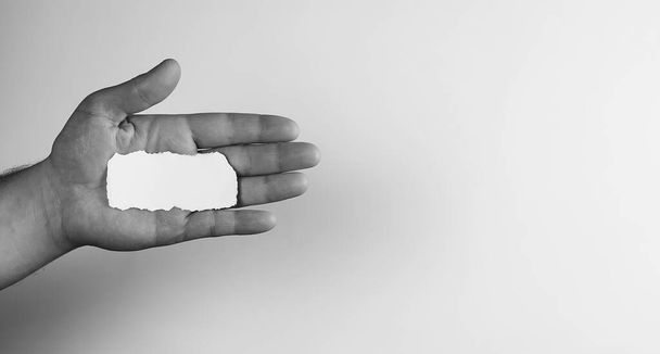 μικρό λευκό κομμάτι χαρτί στο χέρι του άνθρωπος μονόχρωμη - Φωτογραφία, εικόνα