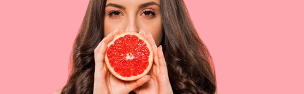 panoramic shot of woman in swimsuit covering face with half of grapefruit isolated on pink  - Foto, Imagem