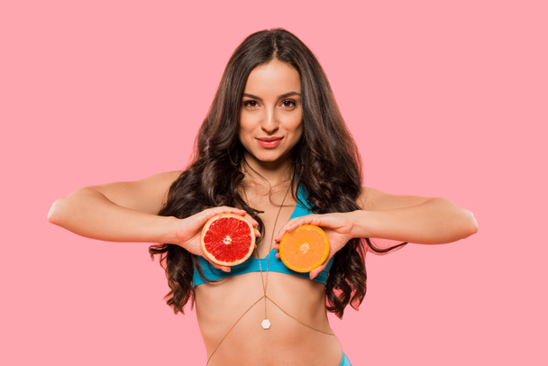 aantrekkelijke vrouw met helften van sinaasappel en grapefruit geïsoleerd op roze  - Foto, afbeelding