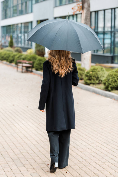 visszapillantás üzletasszony fekete kabátban séta és gazdaság esernyő  - Fotó, kép
