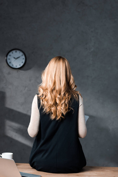 back view of blonde businesswoman sitting on table in office  - Valokuva, kuva