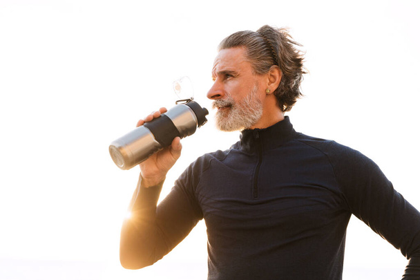 Image of sporty elderly man drinking water while working out - Photo, image