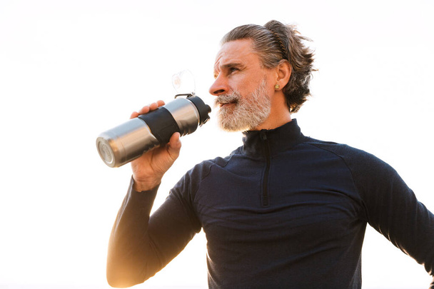 Image of elderly man drinking water from bottle while working out - Foto, Bild