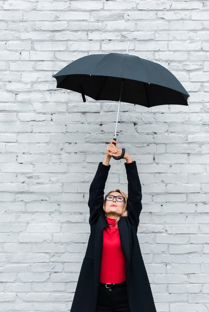 attractive and blonde businesswoman in black coat holding umbrella  - Zdjęcie, obraz