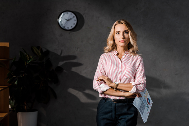 attractive and blonde businesswoman in shirt holding papers in office  - Valokuva, kuva