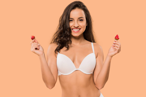cheerful woman in white underwear holding red strawberries isolated on beige  - Foto, Imagem