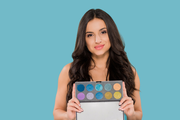 cheerful woman holding eye shadow palette isolated on blue  - Photo, Image