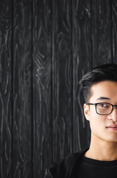 oříznutý pohled na asijského muže v brýlích dívá pryč na dřevěném pozadí  - Fotografie, Obrázek