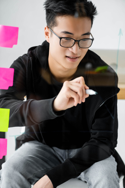 улыбающийся азиатский менеджер в очках, рисующий стрелки на стекле
 - Фото, изображение