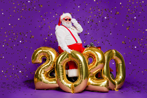 Ho-ho-ho. Full body photo of santa man sit on motorbike big air newyear 2020 balloons saying congratulations wear sun specs x-mas costume isolated purple background - Photo, image