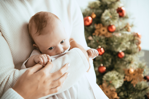 cropped view of father holding adorable baby near christmas tree - Photo, Image