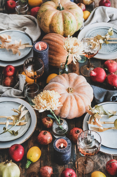 Fall table setting for Thanksgiving day or family gathering dinner. Plates, silverware, floral and fruits decoration, candles and pumpkins over rustic wooden table background - Valokuva, kuva