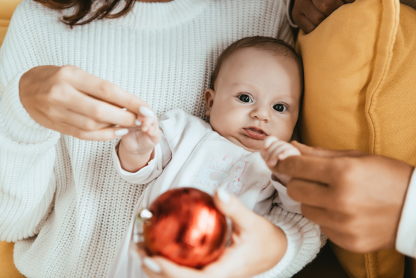 rajattu näkymä äiti ja isä koskettaa käsiä söpö pieni tytär katselee joulupallo
 - Valokuva, kuva