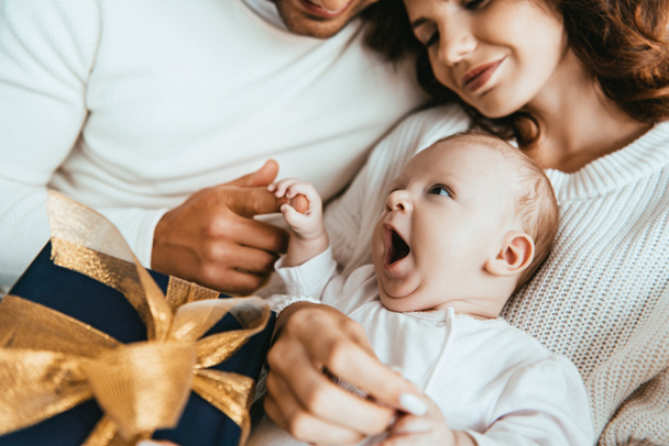 abgeschnittene Ansicht der Eltern mit entzückenden kleinen Baby in der Nähe Geschenkbox mit goldener Schleife - Foto, Bild