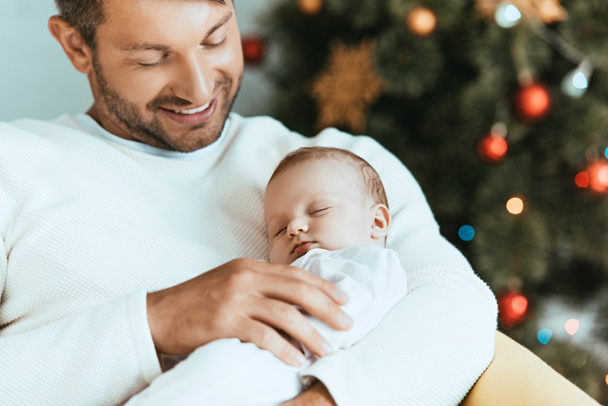 smiling father holding sleeping baby near christmas tree - Photo, Image