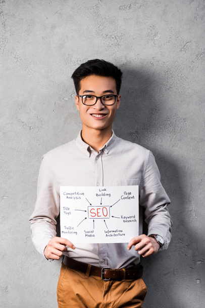 lächelnder asiatischer SEO-Manager hält Papier mit den Worten SEO  - Foto, Bild