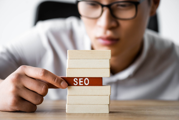 selective focus of asian seo manager holding wooden rectangle with lettering seo  - Foto, afbeelding