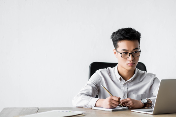 asiatischer SEO-Manager hält Bleistift in der Hand und schaut während des Webinars auf Laptop  - Foto, Bild