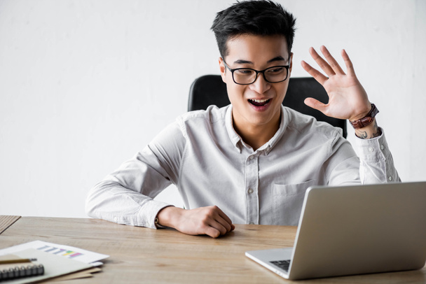 улыбающийся менеджер азиатского SEO, машущий во время вебинара в офисе
  - Фото, изображение