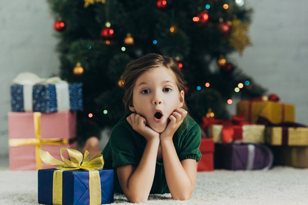 surprised child lying on floor near gift box and looking at camera - Photo, Image
