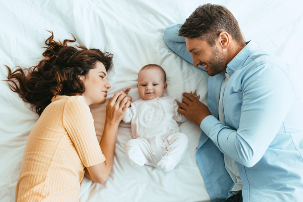 Mutlu anne ve baba, beyaz yatakta yatarken tatlı bebeğe nazikçe dokunuyor. - Fotoğraf, Görsel