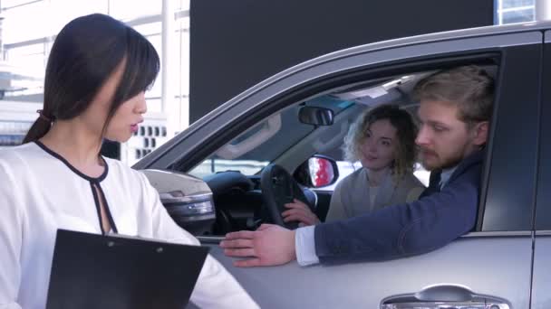 Prodavač asijské žena konzultace se spotřebiteli mladá rodina sedí v autosalonu při nákupu auta na showroom - Záběry, video