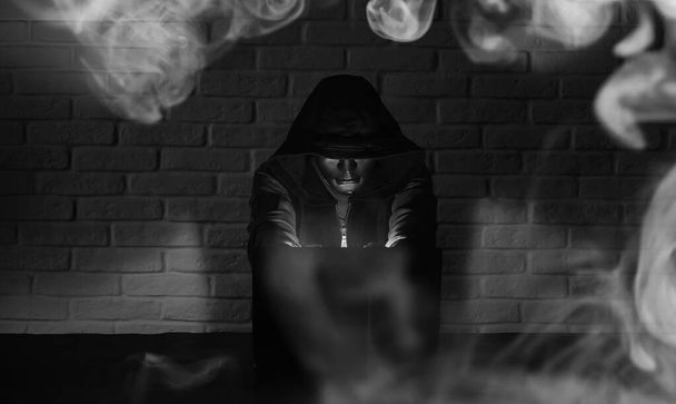 Hacker mit schwarzer Maske und Kapuze am Tisch - Foto, Bild