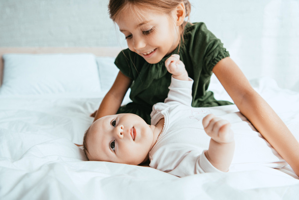 lachend kind kijken naar schattige baby liggend op wit beddengoed - Foto, afbeelding