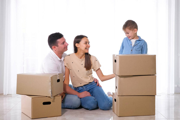 son standing behind boxes near parents sitting on floor - Foto, Imagen
