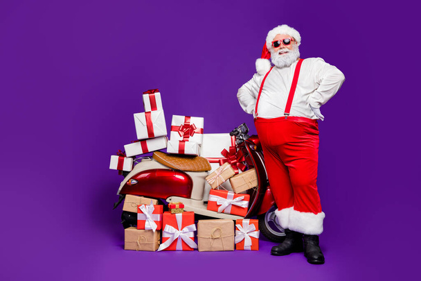Full length photo of fat santa man with many newyear giftboxes on bike advising low final sale prices wear sun specs x-mas costume isolated purple background - Foto, Bild