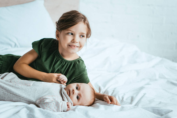smiling child holding hand of little sister lying on white bedding - Zdjęcie, obraz