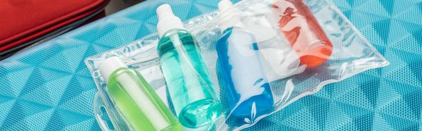 panoramic shot of bright bottles with liquids and cosmetic bag on travel bag  - 写真・画像