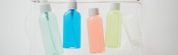 panoramic shot of colorful bottles with liquids in cosmetic bag on white background  - Valokuva, kuva