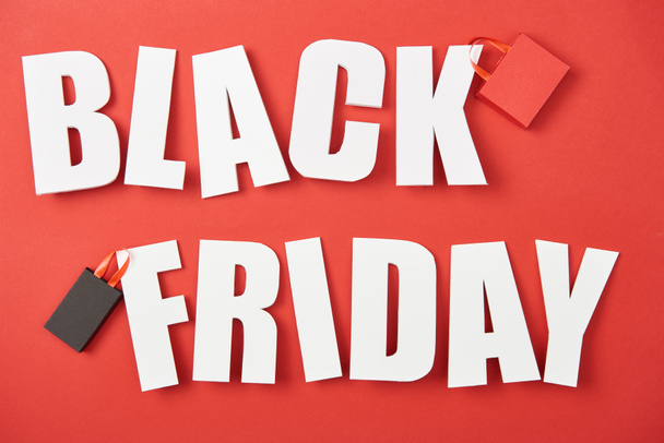 top view of black friday white lettering with shopping bags on red background - Foto, immagini