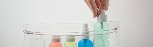 panoramic shot of woman putting bottle with liquid to cosmetic bag on white background  - Foto, immagini