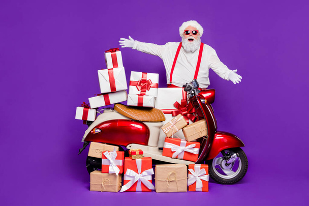 Merry christmas. Photo of fat santa man with many newyear giftboxes on bike congratulating children wear sun specs and red x-mas costume isolated purple background - Photo, image