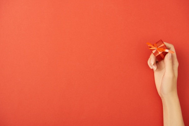 cropped view of woman holding gift box on red background with copy space - Φωτογραφία, εικόνα